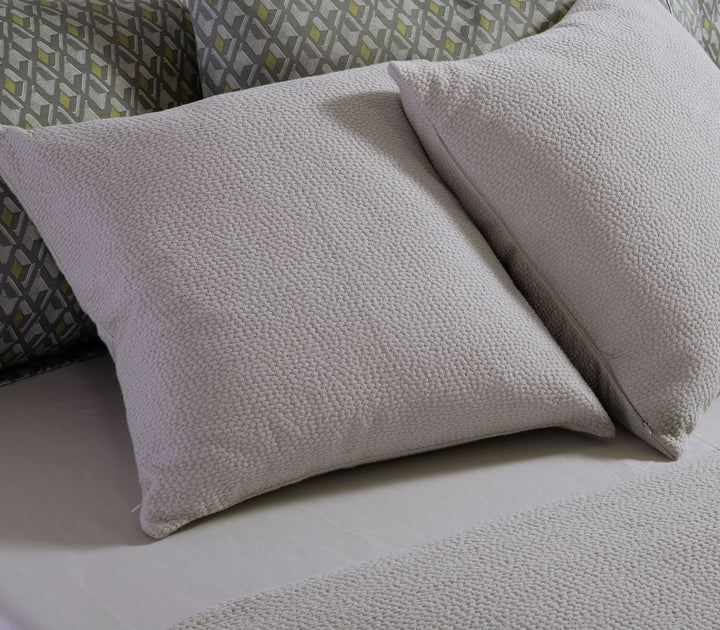 Διακοσμητικές μαξιλαροθήκες Nef-Nef Homeware σε μπεζ απόχρωση τοποθετημένες σε κρεβάτι με γεωμετρικά σεντόνια.