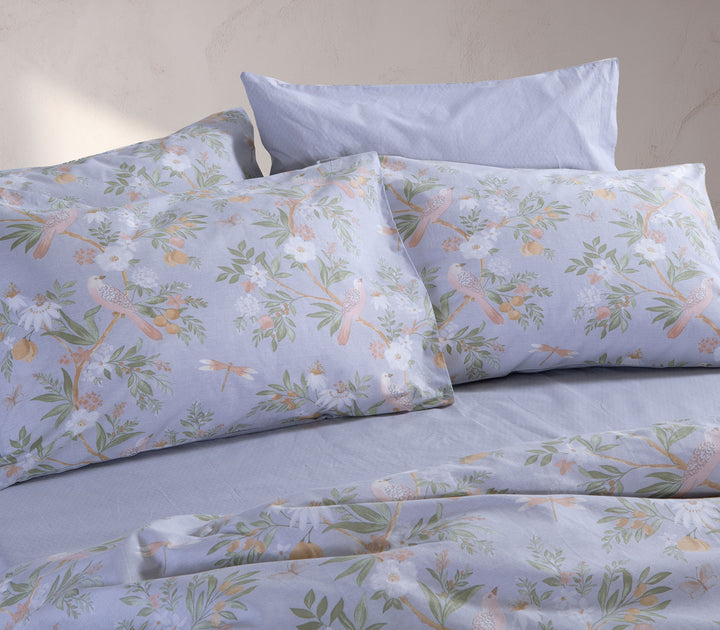 Κρεβάτι στρωμένο με μαξιλαροθήκες Dreamel σε γαλάζιο φλοράλ σχέδιο με πουλάκια και απαλά φυσικά χρώματα.