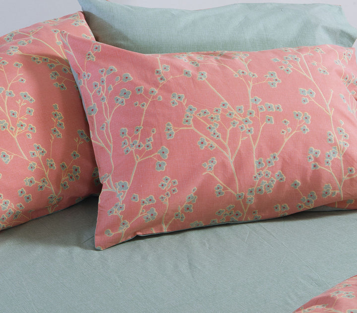 Κοραλί βαμβακερή μαξιλαροθήκη Nef-Nef Homeware με φλοράλ σχέδιο πάνω σε στρωμένο κρεβάτι με γαλάζιο σεντόνι.