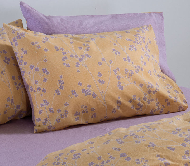 Μουσταρδί βαμβακερή μαξιλαροθήκη Nef-Nef Homeware με φλοράλ μοτίβο τοποθετημένη σε κρεβάτι με λιλά σεντόνι.