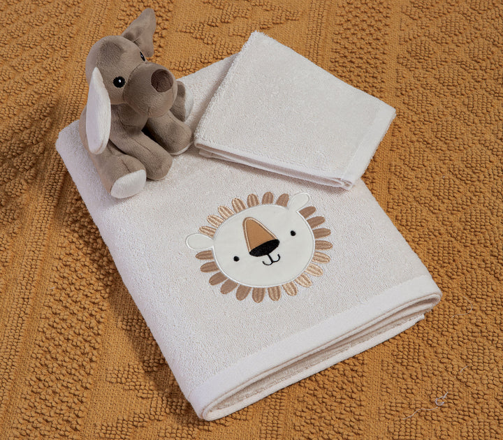 Σετ εκρού βρεφικών πετσετών με κεντημένο λιονταράκι, τοποθετημένες πάνω σε υφασμάτινο φόντο με λούτρινο παιχνίδι δίπλα.