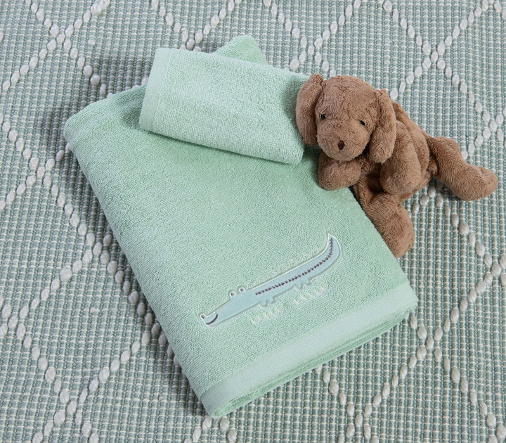 Σετ βρεφικές πετσέτες πράσινες με κεντημένο κροκόδειλο τοποθετημένες σε υφαντό χαλί δίπλα σε λούτρινο παιχνίδι.