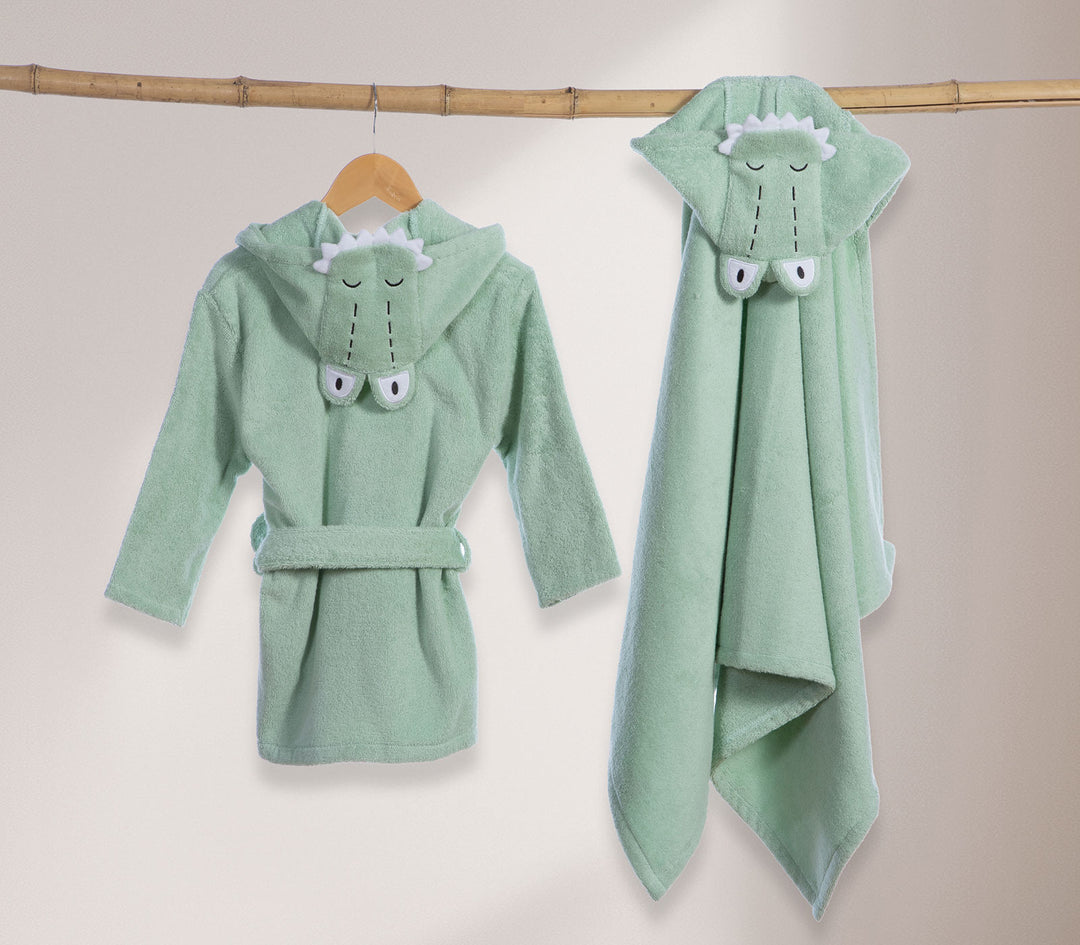 Βρεφικό πράσινο μπουρνούζι με κουκούλα κροκόδειλου και βρεφική κάπα κρεμασμένα σε ξύλινη κρεμάστρα.