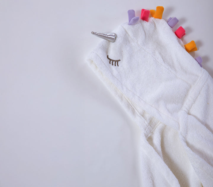 Κοντινή λήψη σε λευκή βρεφική κάπα μπάνιου με κουκούλα και σχέδιο μονόκερου σε απαλό λευκό φόντο.