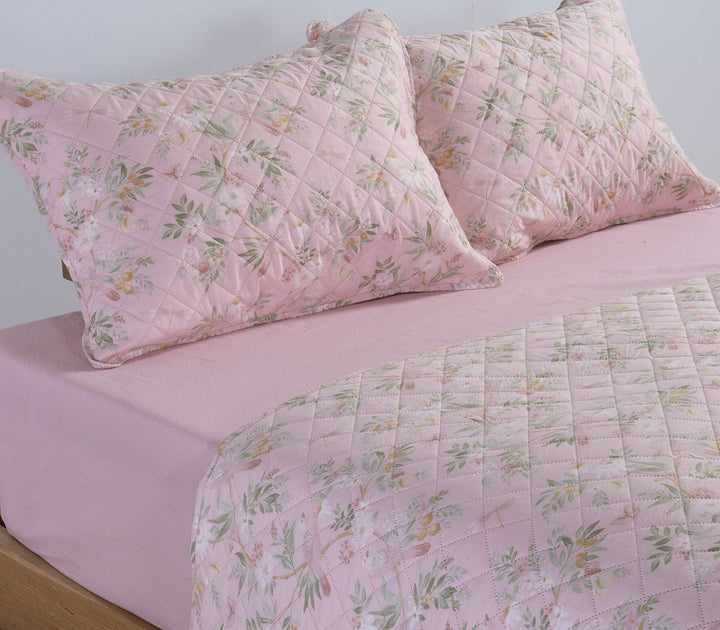 Κρεβάτι με ροζ κουβερλί Dreamel και διακοσμητικές μαξιλαροθήκες με φλοράλ μοτίβο πάνω σε ροζ κατωσέντονο.
