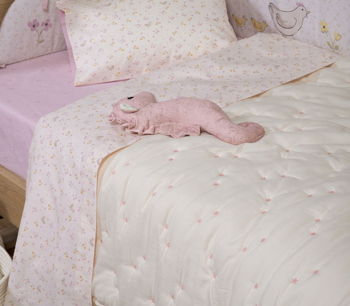 Βρεφικό κρεβατάκι με εκρού κουβερλί με μικρά ροζ λουλουδάκια και διακοσμητικό παιχνίδι.