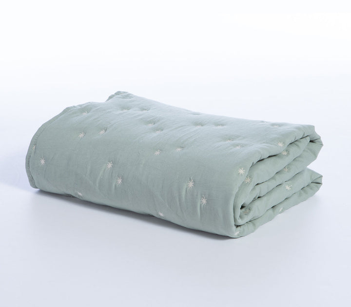 Διπλωμένο βρεφικό κουβερλί σε μέντα απόχρωση με μικρά λευκά κεντημένα αστέρια σε λευκό φόντο.