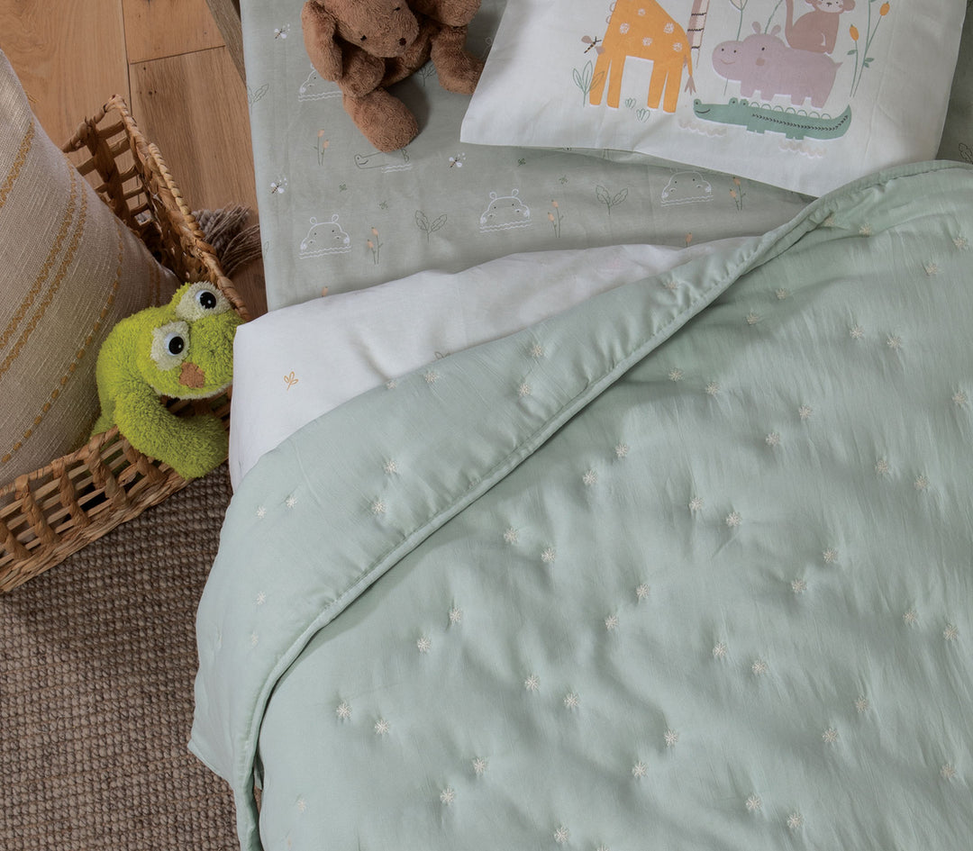 Βρεφικό κρεβατάκι με μέντα κουβερλί με μικρά κεντημένα αστέρια και μαξιλάρι με ζωάκια σε παιδικό δωμάτιο.