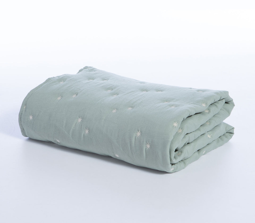 Διπλωμένο βρεφικό κουβερλί σε μέντα απόχρωση με μικρά λευκά κεντημένα αστέρια σε λευκό φόντο.