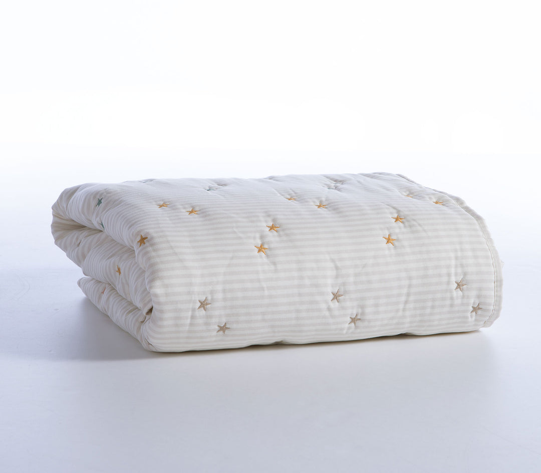 Διπλωμένο βρεφικό κουβερλί σε εκρού απόχρωση με μικρά κεντημένα αστέρια σε λευκό φόντο.