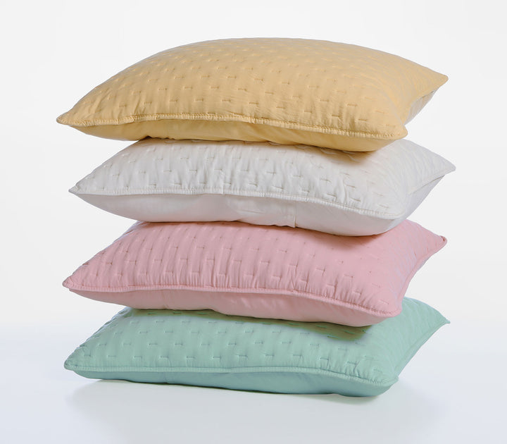 Στοίβα από διακοσμητικές μαξιλαροθήκες σε παστέλ αποχρώσεις κίτρινο, λευκό, ροζ και τιρκουάζ με καπιτονέ υφή.