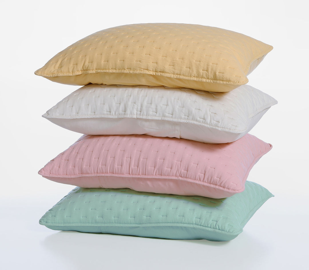 Στοίβα από διακοσμητικές μαξιλαροθήκες σε παστέλ αποχρώσεις κίτρινο, λευκό, ροζ και τιρκουάζ με καπιτονέ υφή.