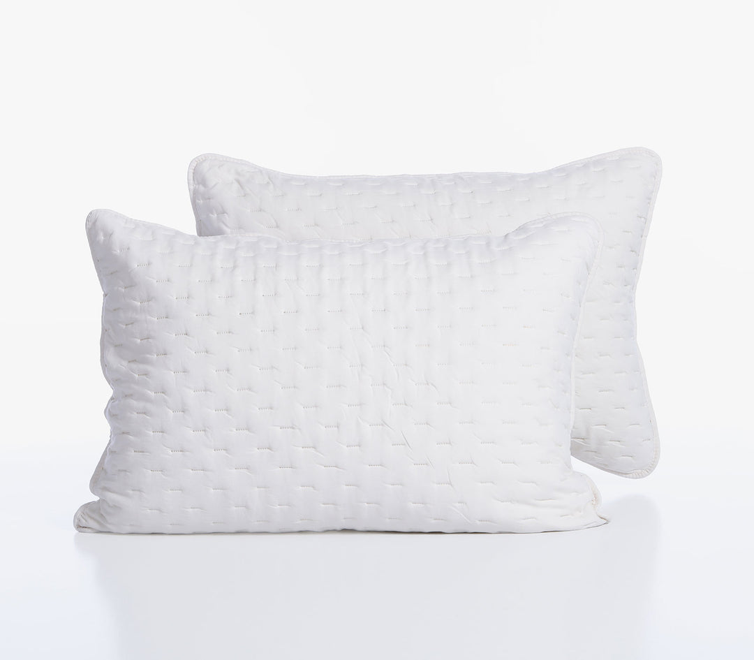 Δύο λευκές διακοσμητικές μαξιλαροθήκες με διακριτικό καπιτονέ σχέδιο τοποθετημένες η μία μπροστά από την άλλη.