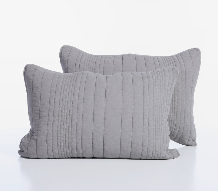 Δύο γκρι βαμβακερές καπιτονέ μαξιλαροθήκες τοποθετημένες η μία μπροστά από την άλλη σε λευκό φόντο.