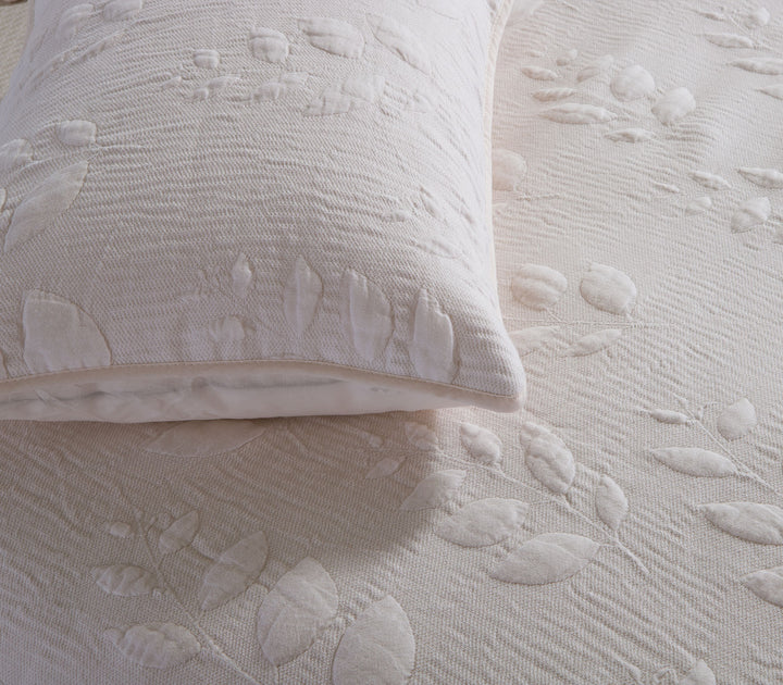 Σετ εκρού διακοσμητικών μαξιλαροθηκών με ανάγλυφο μοτίβο φύλλων σε κρεβάτι.