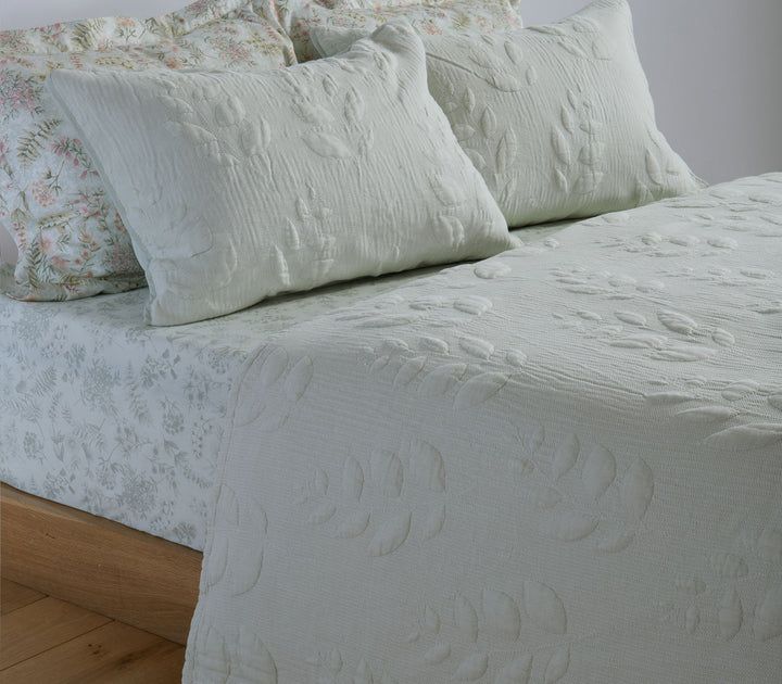 Σετ πράσινων διακοσμητικών μαξιλαροθηκών με ανάγλυφο φυλλωτό σχέδιο σε στρωμένο κρεβάτι.