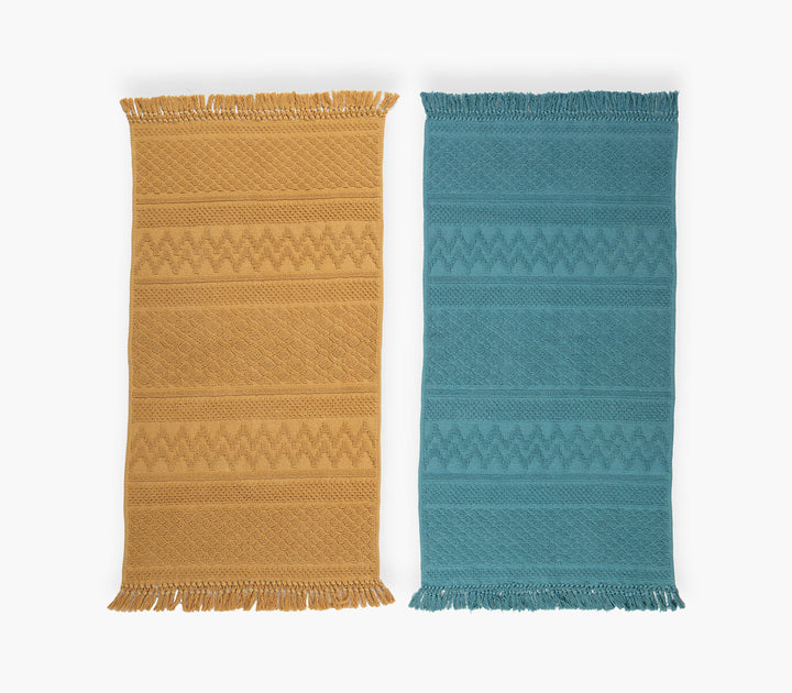 Δύο χαλάκια κουζίνας σε μουσταρδί και τιρκουάζ με γεωμετρικό ζακάρ σχέδιο και κρόσσια σε λευκό φόντο.