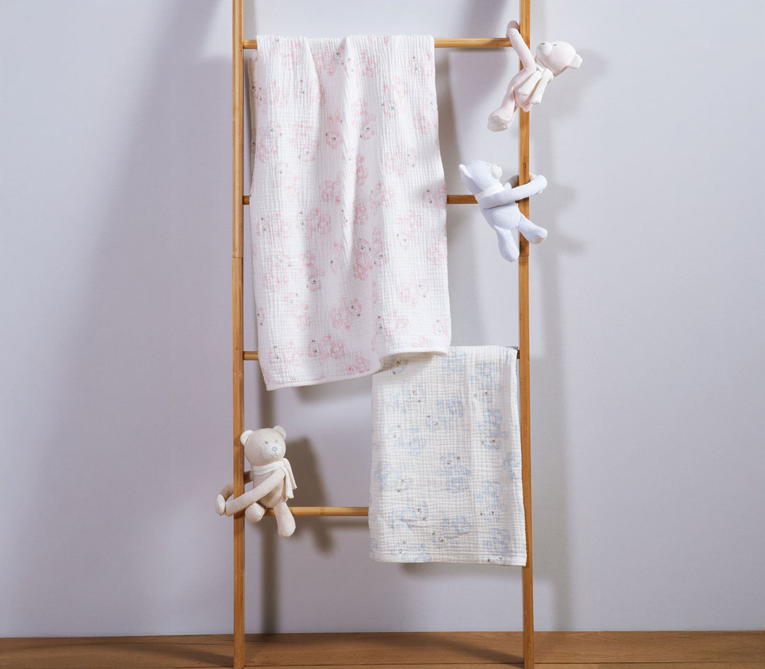 Βρεφικές κουβέρτες αγκαλιάς με σχέδιο αρκουδάκια κρεμασμένες σε ξύλινη σκάλα διακόσμησης σε παιδικό δωμάτιο.