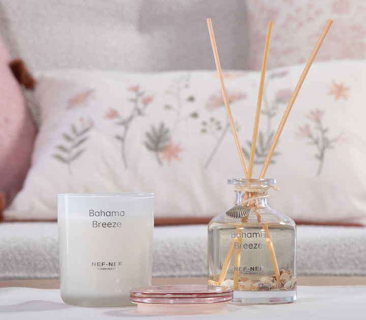 Αρωματικό κερί Bahama Breeze της Nef-Nef Homeware σε γυάλινο δοχείο δίπλα σε diffuser με στικς πάνω σε τραπεζάκι.