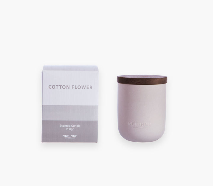 Αρωματικό χώρου με στικς Cotton Flower της Nef-Nef Homeware δίπλα σε αρωματικό κερί πάνω σε ψάθινο σουπλά σε καναπέ.