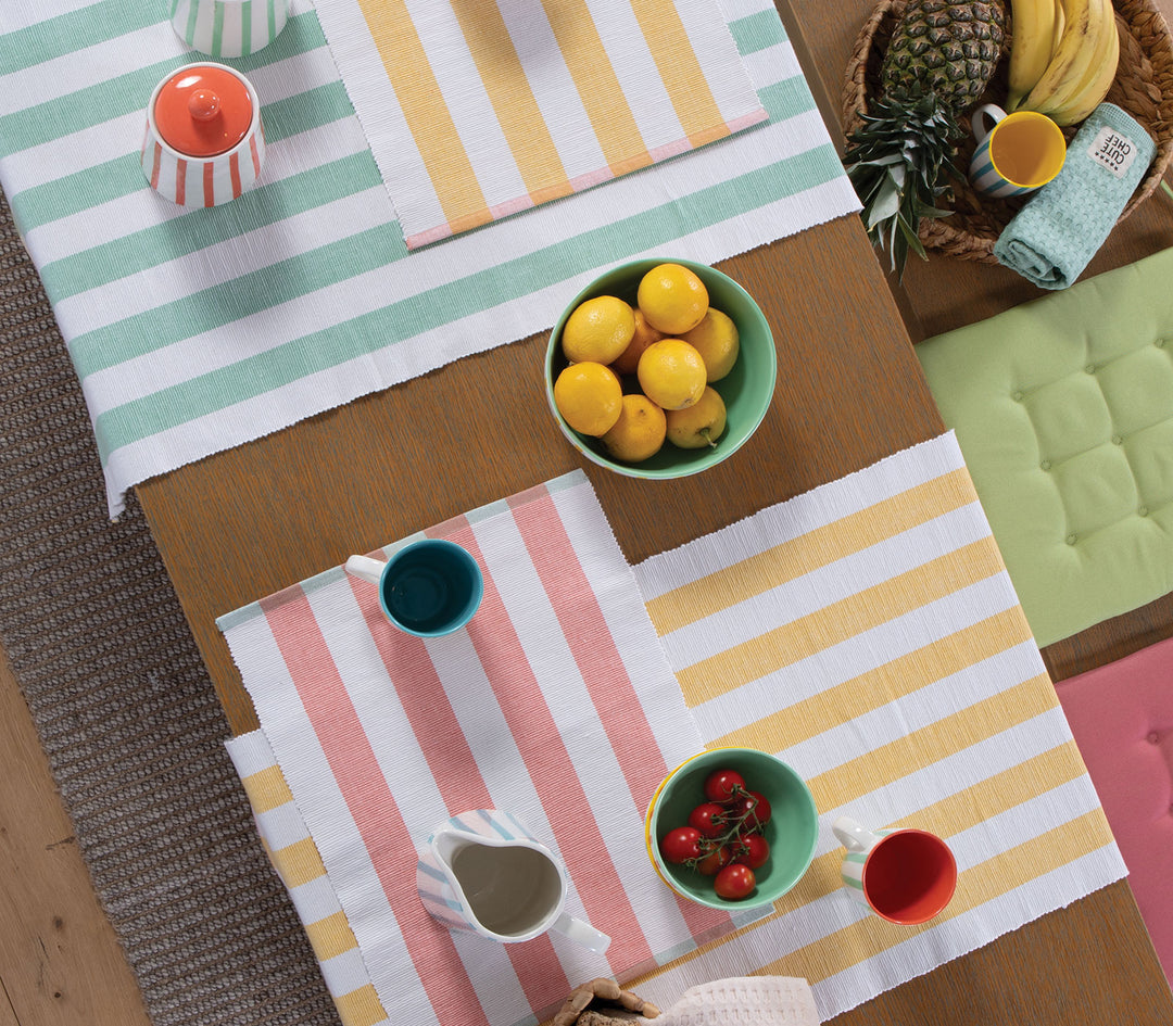 Σύνθεση τραπεζιού με ριγέ σουπλά σε κοραλί, κίτρινο και πράσινο με μπολ, φρούτα και φλιτζάνια.