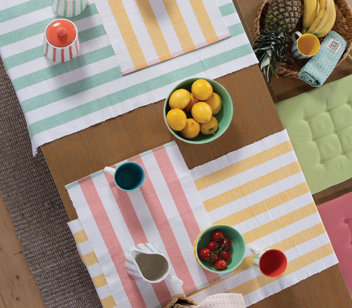 Σύνθεση τραπεζιού με ριγέ σουπλά σε κοραλί, κίτρινο και πράσινο με μπολ, φρούτα και φλιτζάνια.