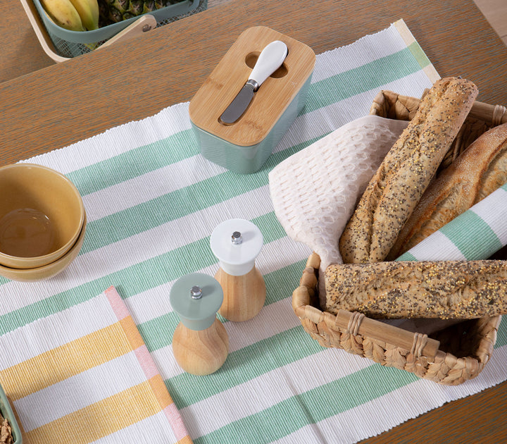 Τραπέζι με πράσινη ριγέ τραβέρσα, καλάθι με ψωμί και διακοσμητικά κουζίνας σε φυσικό φόντο.