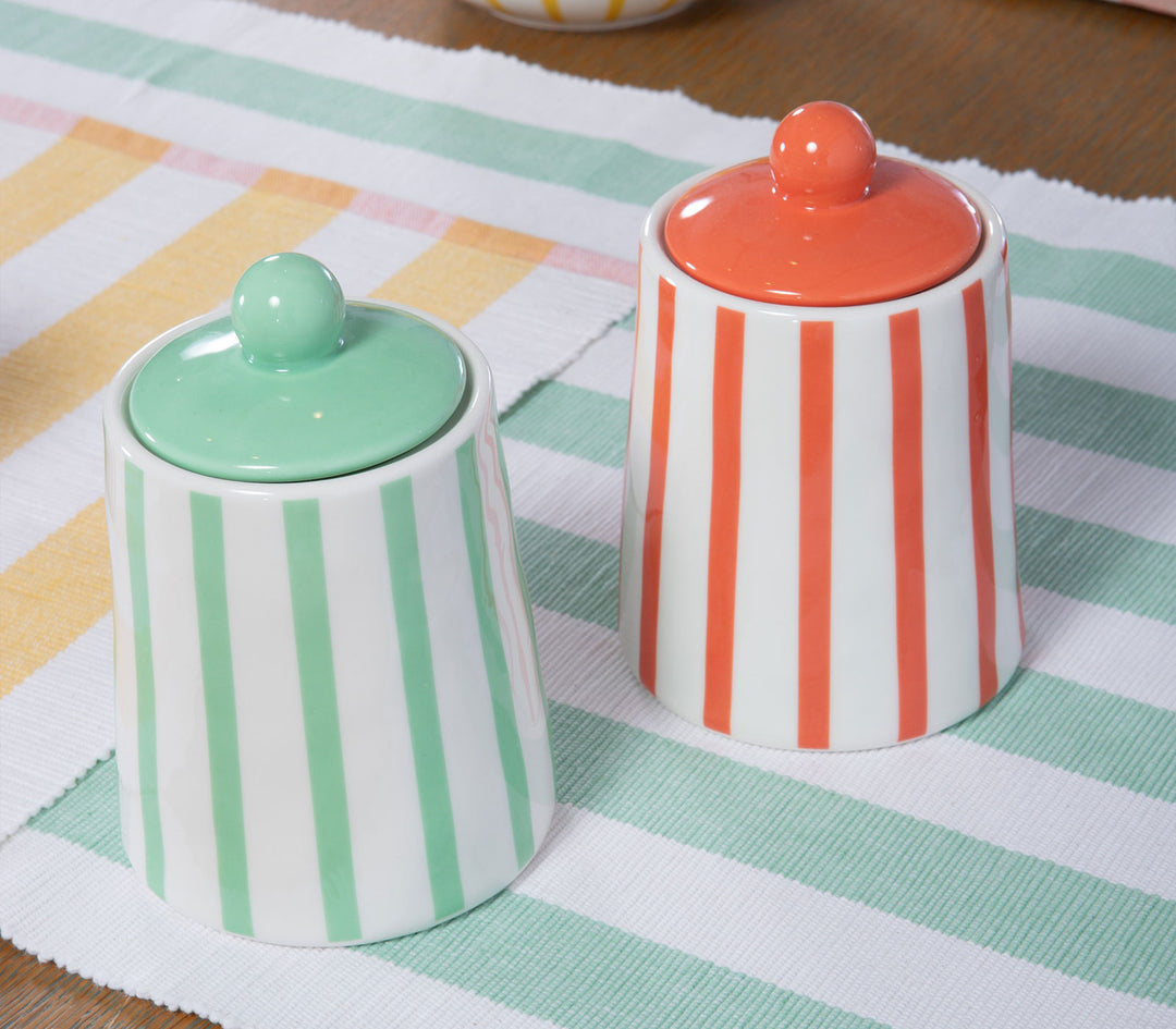 Δύο κεραμικά βάζα με καπάκι σε ριγέ σχέδιο πάνω σε τραπέζι με παστέλ ριγέ τραπεζομάντηλο.