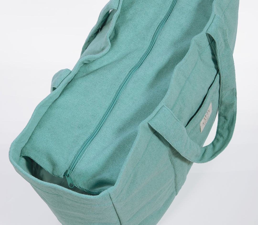 Κοντινό σε τιρκουάζ τσάντα θαλάσσης με φερμουάρ και μαλακή υφή υφάσματος σε ουδέτερο φόντο.