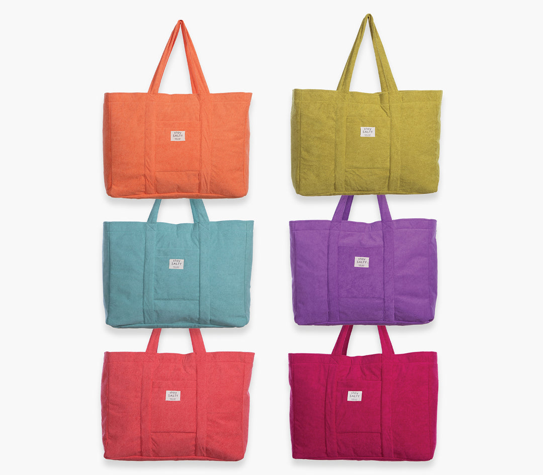 Συλλογή μονόχρωμων τσαντών θαλάσσης σε διαφορετικά χρώματα τοποθετημένες σε ουδέτερο φόντο.