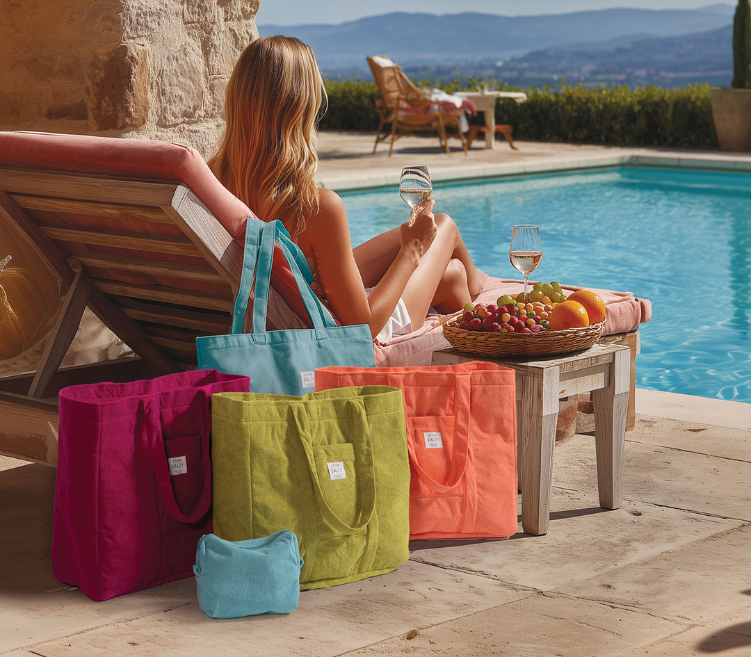 Πολύχρωμες τσάντες θαλάσσης δίπλα σε πισίνα με φρούτα και καλοκαιρινό σκηνικό χαλάρωσης.