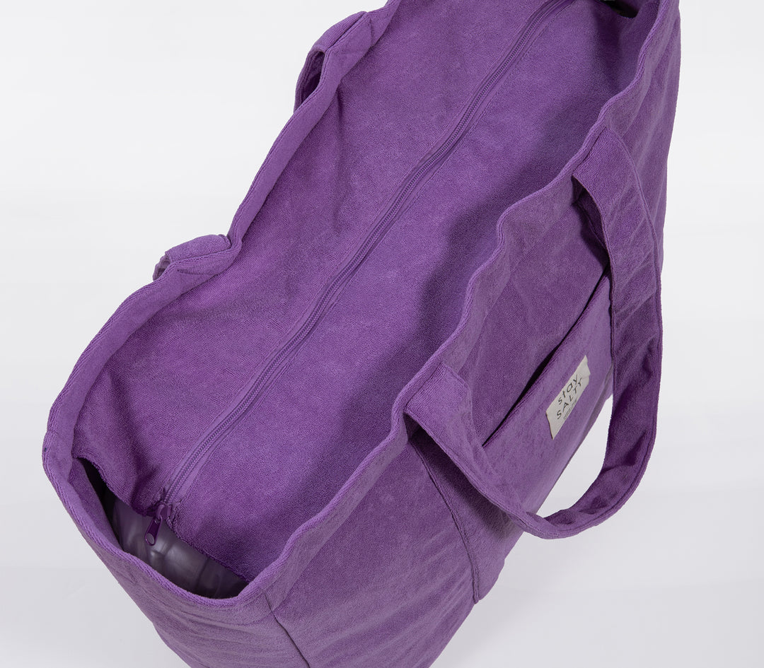 Κοντινό σε μωβ τσάντα θαλάσσης με φερμουάρ και μαλακή υφή υφάσματος σε ουδέτερο φόντο.