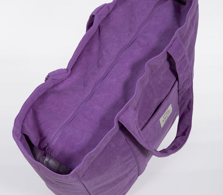 Κοντινό σε μωβ τσάντα θαλάσσης με φερμουάρ και μαλακή υφή υφάσματος σε ουδέτερο φόντο.