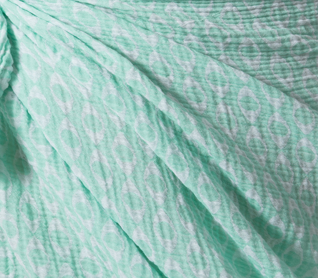Κοντινή λήψη σε τιρκουάζ βαμβακερό παρεό με ανάγλυφη υφή και λευκό μοτίβο.