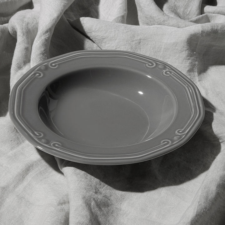 Γκρι βαθύ πιάτο με ανάγλυφο σχέδιο τοποθετημένο πάνω σε γκρι λινό ύφασμα σε φυσικό φωτισμό.