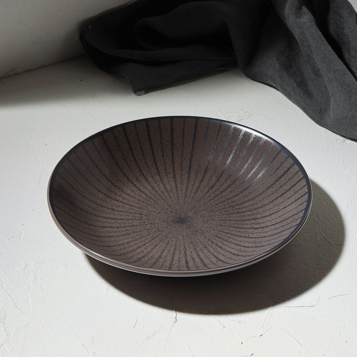 Ρηχό πιάτο Nordic Estia σε σκούρο γκρι χρώμα με ακτινωτό ανάγλυφο σχέδιο, τοποθετημένο με λινό ύφασμα.