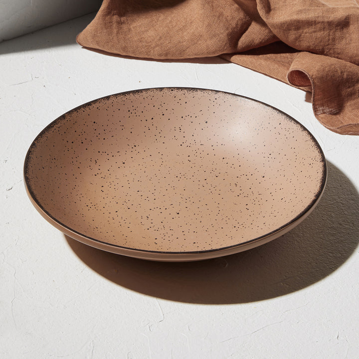 Ρηχό πιάτο Terra τερακότα της Estia σε σκηνικό με φυσικό φως και λινό ύφασμα σε γήινους τόνους στο φόντο.