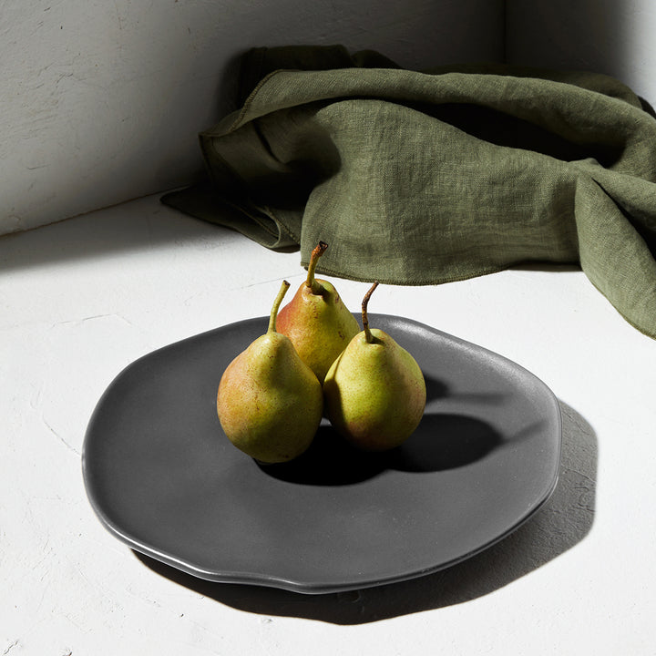 Πιάτο σε σκηνικό με λινό ύφασμα και τρία αχλάδια στο κέντρο, σε φυσικό φωτισμό.