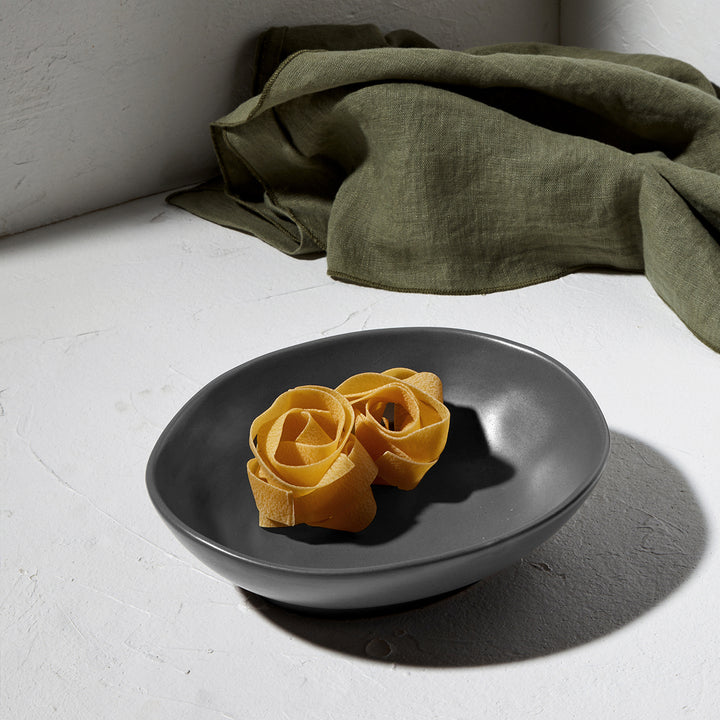 Πιάτο γραφίτη με στρογγυλεμένες γραμμές και διακριτική υφή, μερικώς γεμάτο με στριφτές ταλιατέλες.