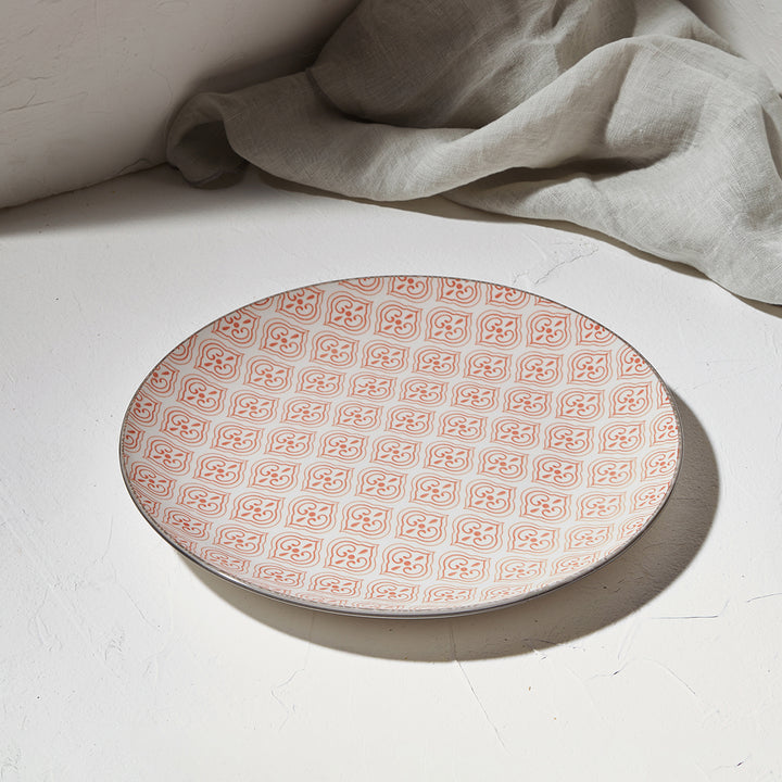 Ρηχό πιάτο με κοραλί μοτίβο σε τραπέζι με λευκή επιφάνεια και μπεζ λινό ύφασμα στο φόντο.