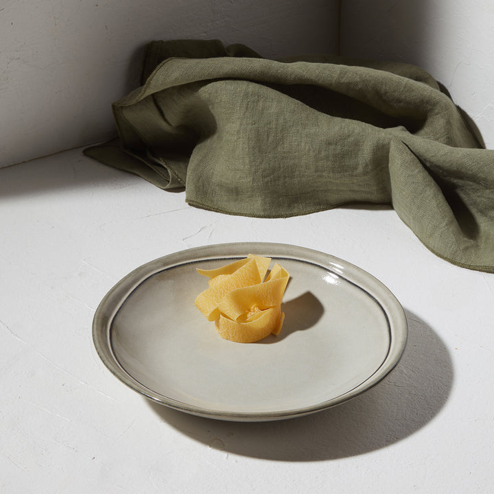 Πιάτο βαθύ Deline γκρι απόχρωσης με αβοκάντο σε λευκή επιφάνεια και πράσινο ύφασμα στο φόντο.