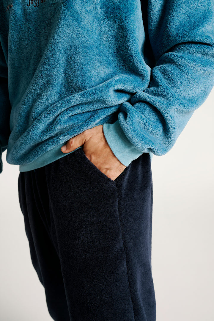 Κοντινό πλάνο σε ανδρικό fleece σετ πιτζάμας με μπλούζα σε ανοιχτό μπλε και σκούρο μπλε παντελόνι, όπου φαίνεται το χέρι του άνδρα μέσα στην τσέπη, σε ουδέτερο φόντο