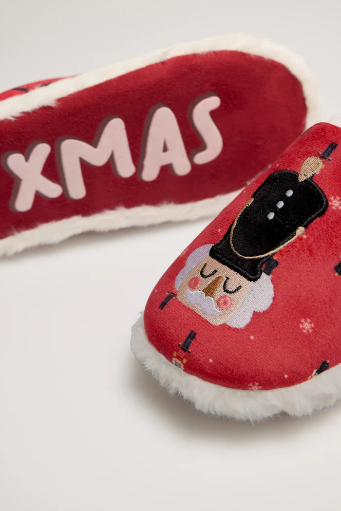 Κοντινή λήψη κόκκινης παντόφλας με σχέδιο καρυοθραύστη και λευκή επένδυση, με φόντο τη σόλα που γράφει “XMAS