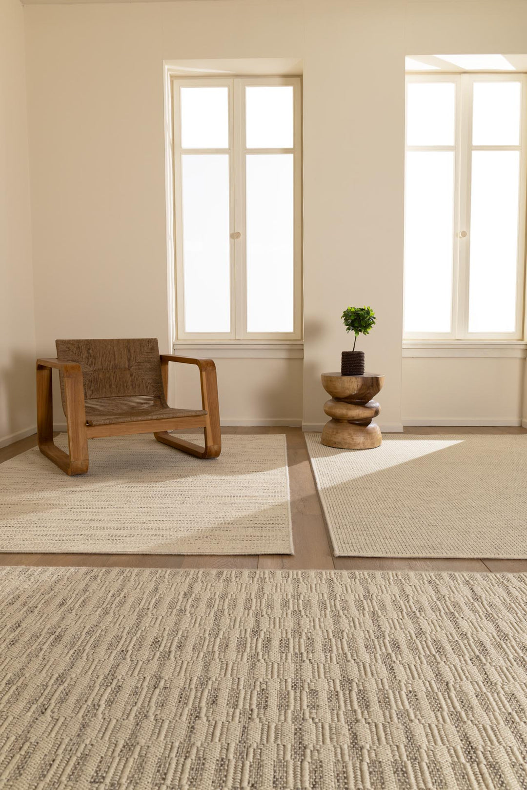 Μοντέρνα χαλιά σε ουδέτερες αποχρώσεις διακοσμούν φωτεινό, minimal σαλόνι με ξύλινη πολυθρόνα, design τραπεζάκι και φυσικό φως από μεγάλα παράθυρα. Ιδανική διακόσμηση για χαλαρή και φυσική ατμόσφαιρα.