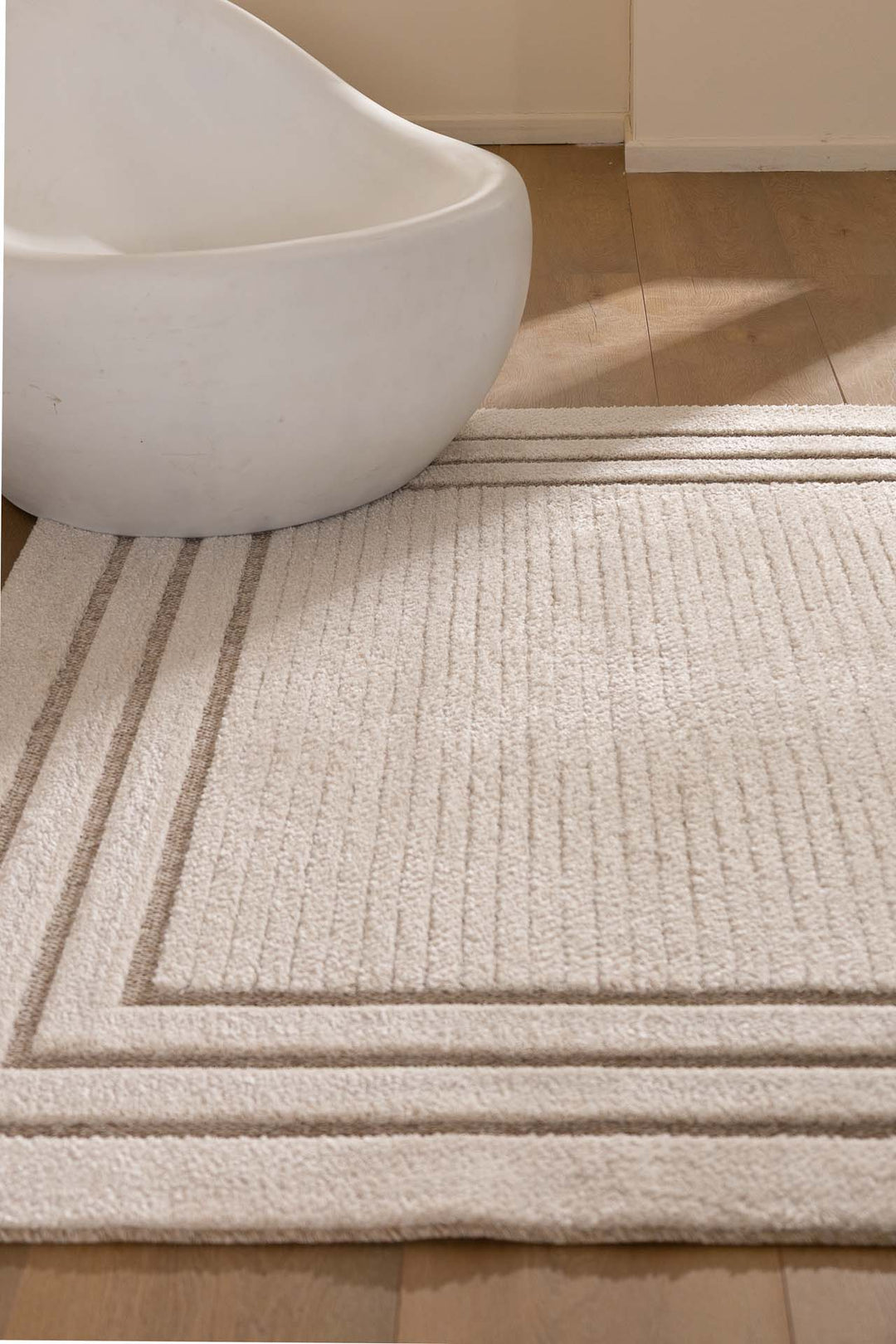 Χαλί σε μπεζ τόνους με πλαίσιο σε γήινες αποχρώσεις, συνδυασμένο με λευκή μοντέρνα καρέκλα σε ξύλινο πάτωμα.