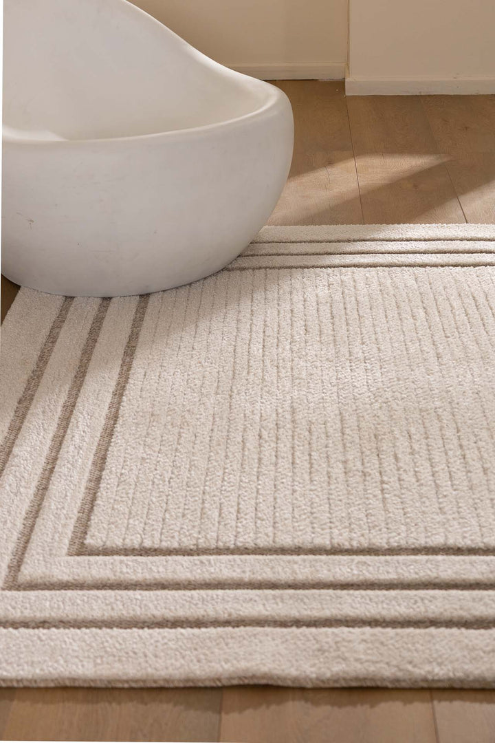 Χαλί σε μπεζ τόνους με πλαίσιο σε γήινες αποχρώσεις, συνδυασμένο με λευκή μοντέρνα καρέκλα σε ξύλινο πάτωμα.