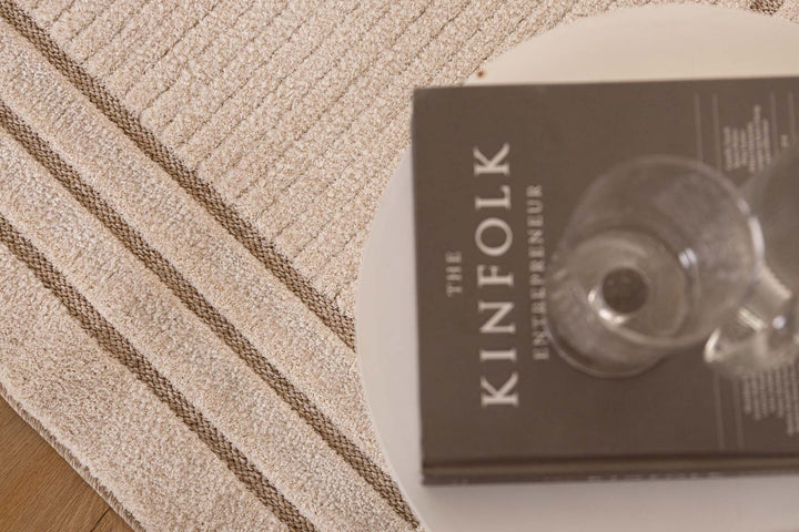 Μοντέρνο χαλί σε μπεζ απόχρωση με διακριτικές γραμμικές λεπτομέρειες, κοντινή λήψη με βιβλίο και ποτήρι σε τραπεζάκι.