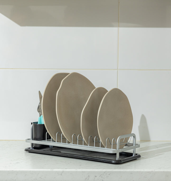 Κοντινή λήψη του στεγνωτήρα από χαμηλή γωνία, τοποθετημένος πάνω στον πάγκο, με τα πιάτα τοποθετημένα κάθετα και τη θήκη των μαχαιροπίρουνων στα αριστερά.