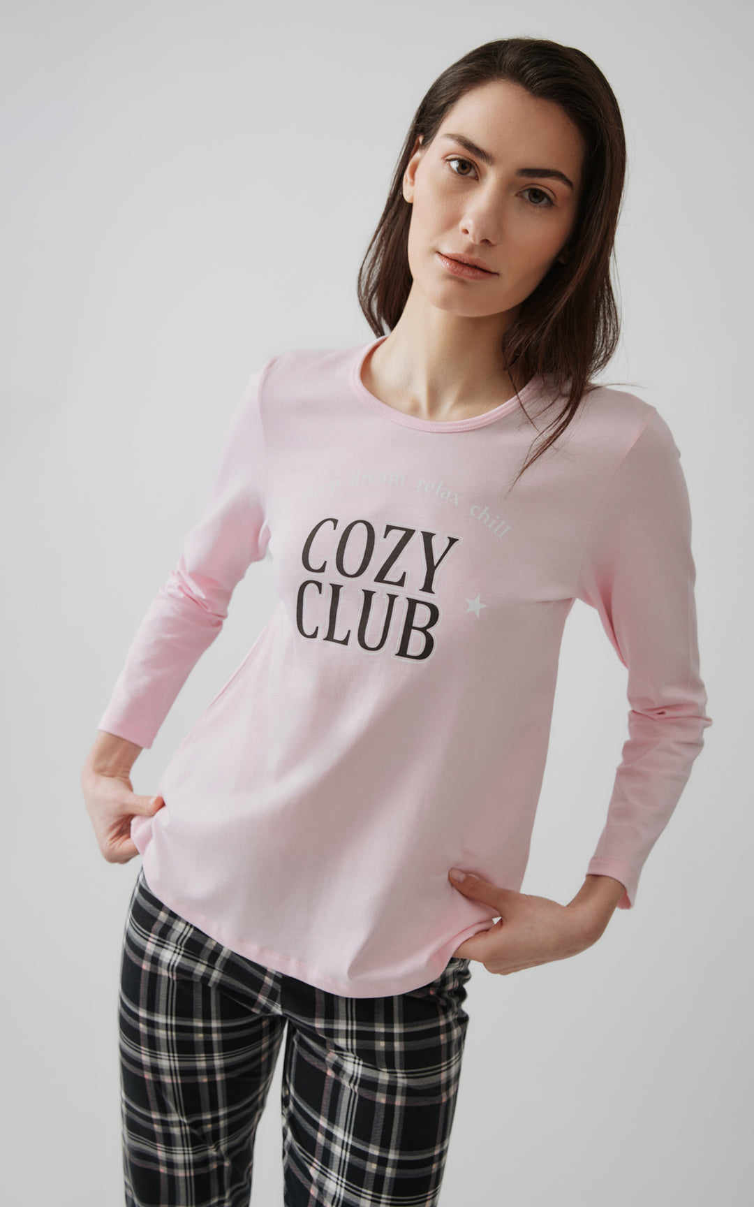 Κοντινό πλάνο από γυναικεία πιτζάμα σε ροζ απόχρωση με μακρυμάνικη μπλούζα που γράφει "Cozy Club" και καρό παντελόνι σε μαύρο, λευκό και ροζ.