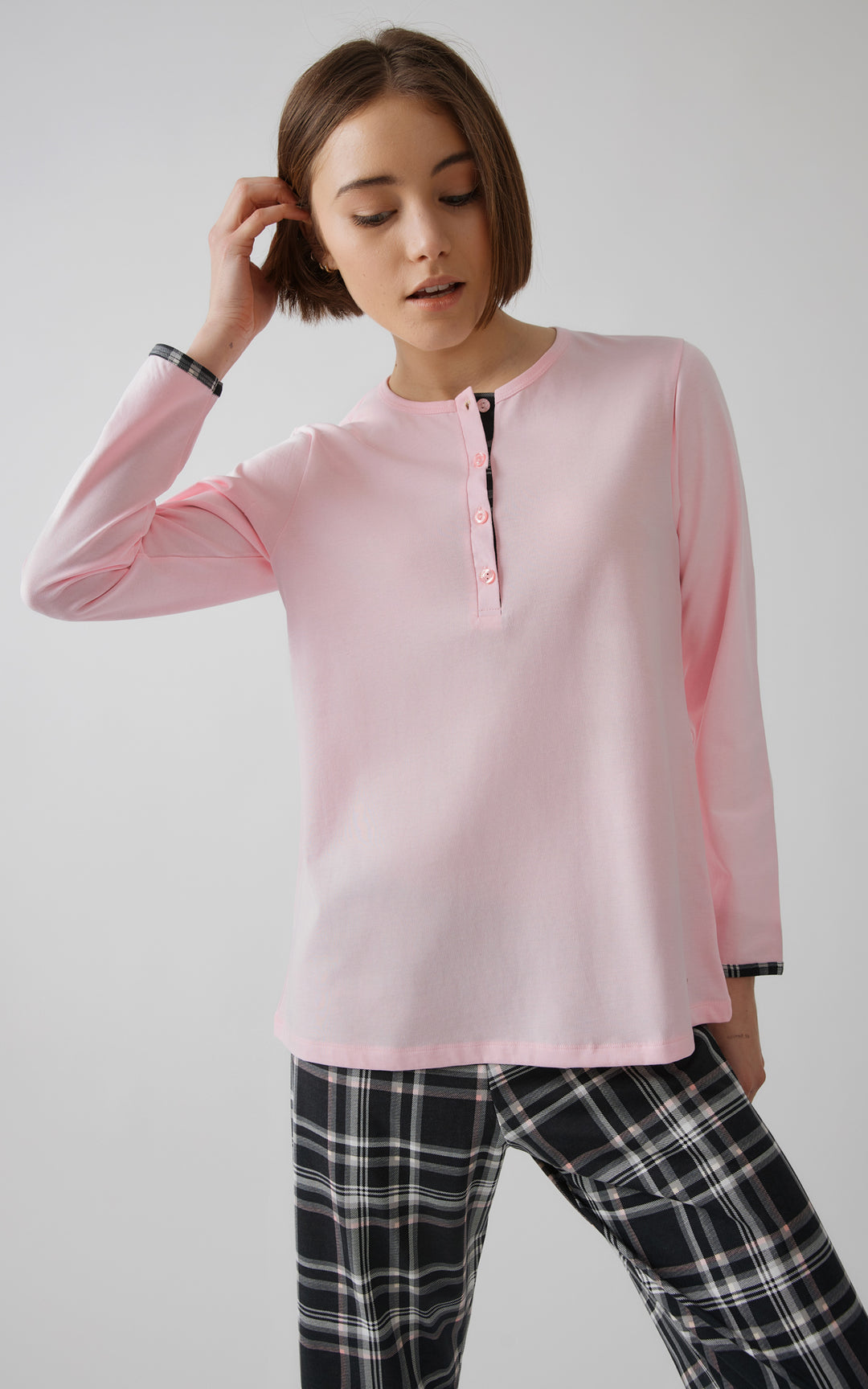 Ολόσωμη λήψη γυναικείας πιτζάμας σε ροζ και μαύρες καρό αποχρώσεις, με μακριά μανίκια και ίσια γραμμή. Το μοντέλο στέκεται χαλαρά σε ουδέτερο φόντο.